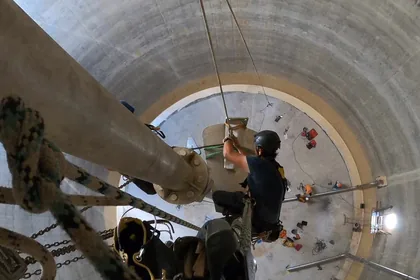 Cordistes à l'intérieur d'un ouvrage cylindrique en béton, autour d'une conduite