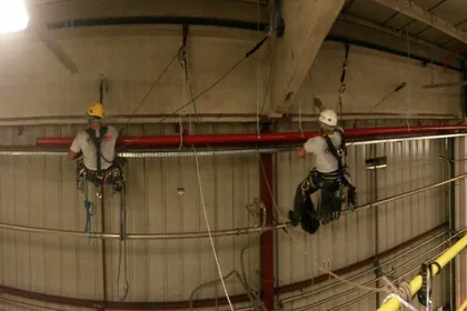 Cordiste suspendu sous la charpente métallique d'un hangar industriel