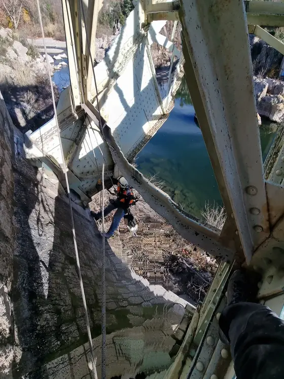 Cordiste progressant sur corde sous un pont au-dessus d'un plan d'eau